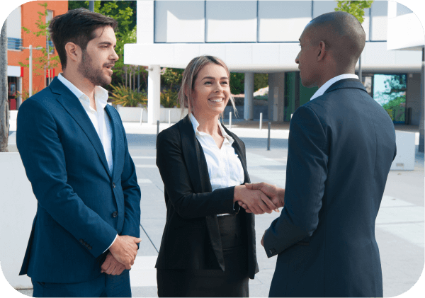 Three business professionals shaking hands in front of a modern office building.